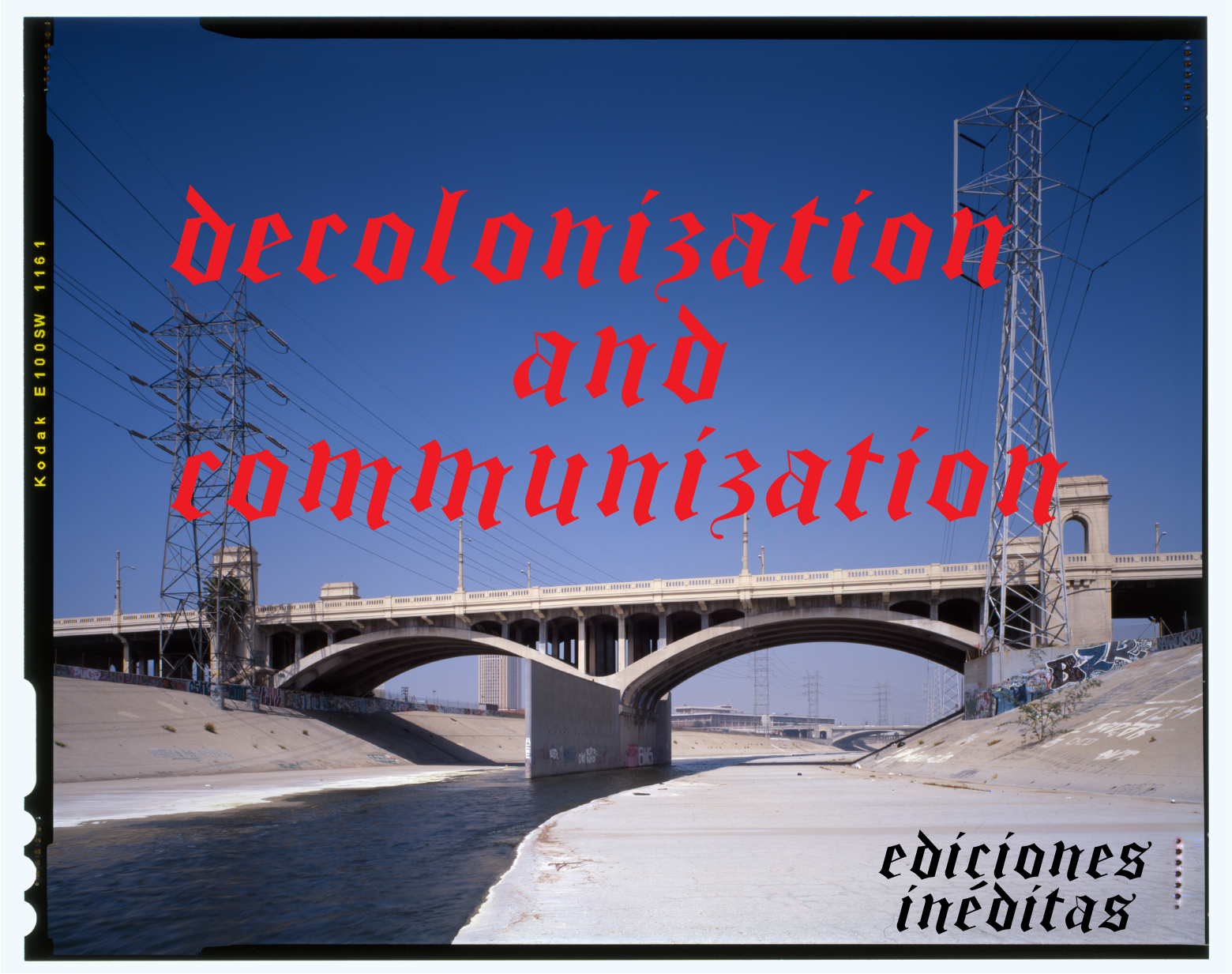 a color film photograph of the previous 6th Street Bridge, seen from the bottom of the channelized Los Angeles River. Water flows down the middle. Power lines and their towers stand before the bridge. In red Old English text reads, "decolonization and communization." At the bottom right-hand side reads "ediciones ineditas" in black Old English text.